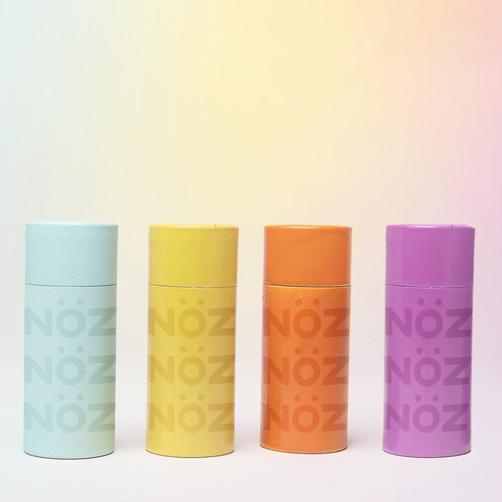 Four Nöz nose sunscreen containers lined up in a row showing the options: blue yellow orange purple